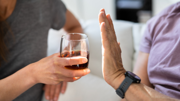 A person refuses a glass of alcohol offered by another person.