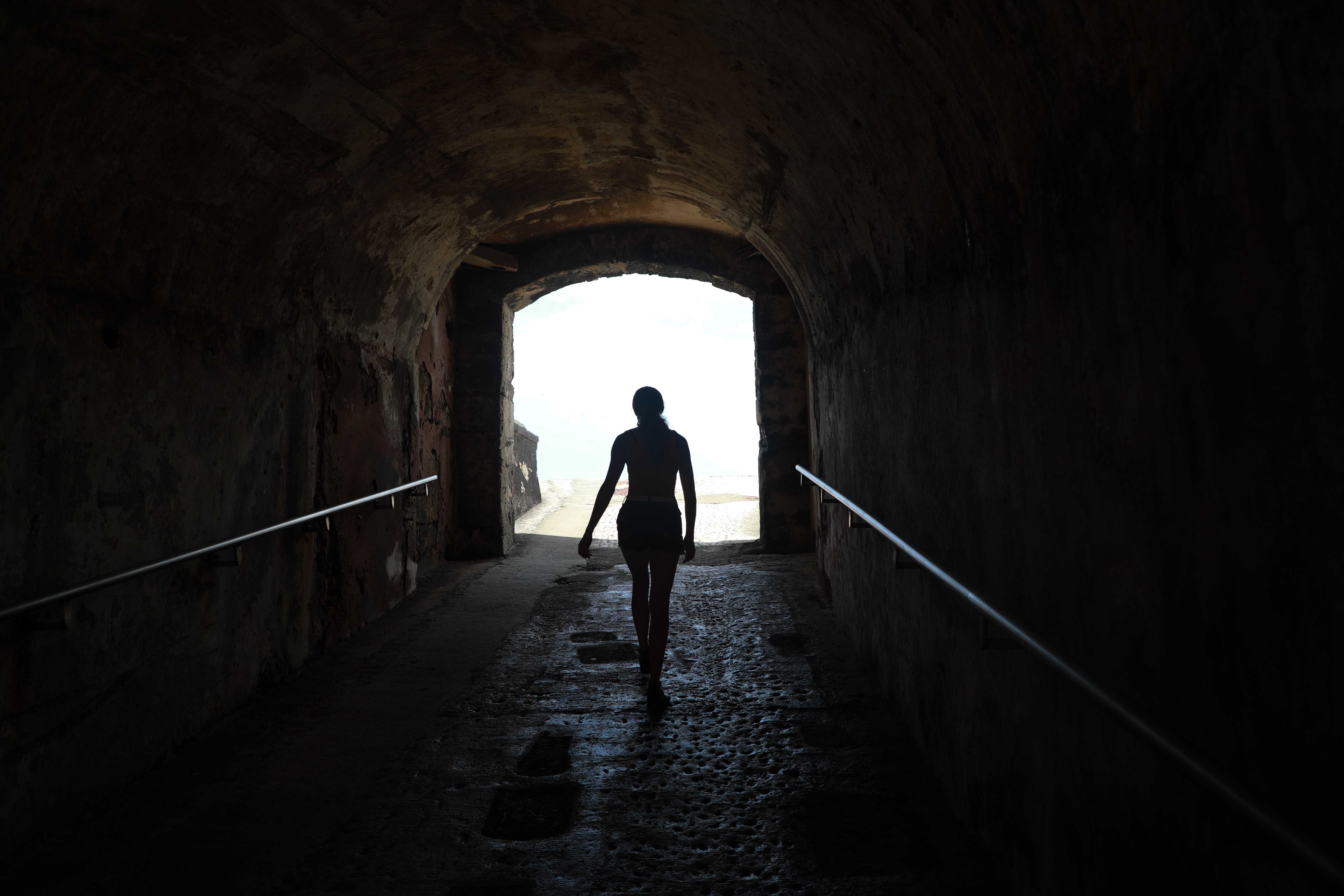 Young woman walking out of dark tunnel on to a beach.