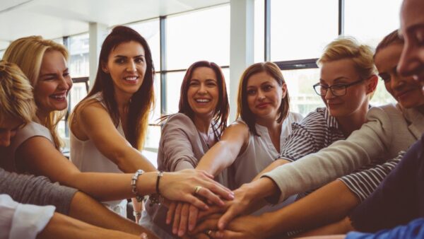 A diverse group of women smile and put their hands together in a circle.