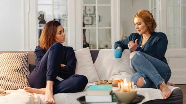 Two female friends speak seriously while sitting on a couch.
