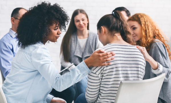 Support group sitting in a circle providing comfort to one of the participants.