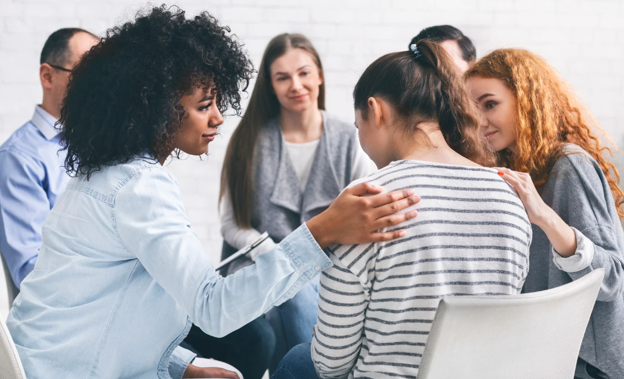 Support group sitting in a circle providing comfort to one of the participants.